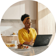 Lady in a yellow jumper sat at her kitchen table on her laptop